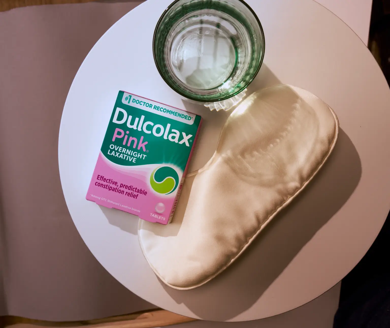 Dulcolax Pink Overnight Laxative tablets beside a glass of water and a sleep mask on a round table.